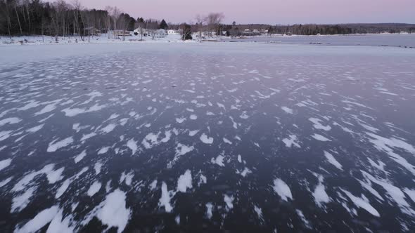 Flying low towards shore above snowy patterns in dark ice at dawn AERIAL