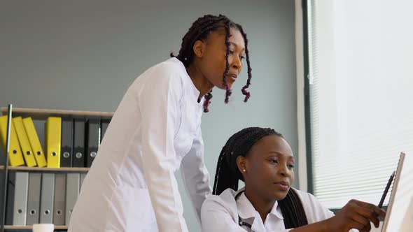 Two African Women Students Discussing Patient Treatment Plan Showing Something on Laptop