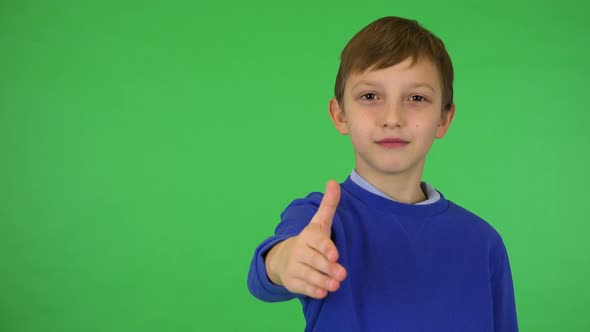 A Young Cute Boy Extends a Hand for a Handshake Toward the Camera - Green Screen Studio