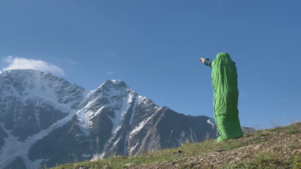 Person in Green Sleeping Bag Jumps Up and Waves Hands