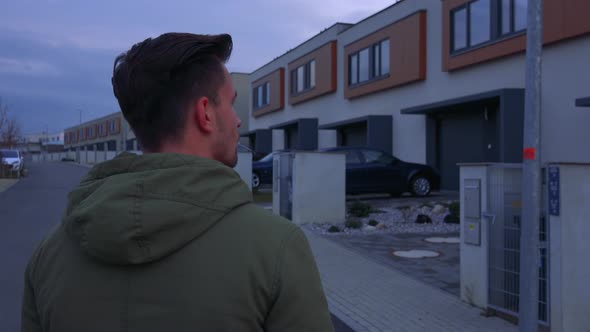 A Young Man Stands with His Back To the Camera on a Road in a Neighborhood and Looks Around