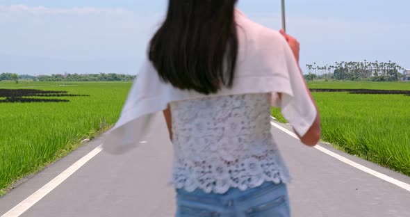 Woman Holding Umbrella and Walking Though the Road with Paddy Rice Beside