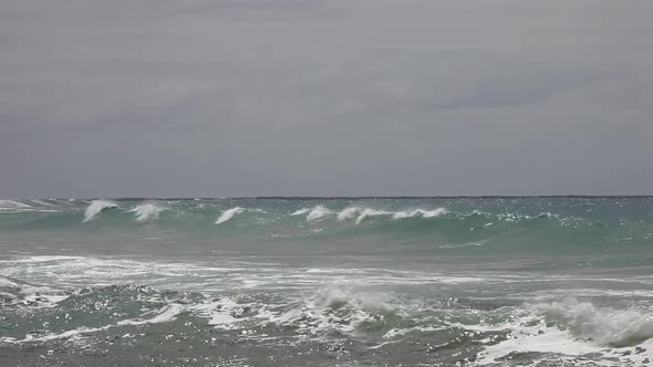 Distant waves rolling in and crashing under overcast sky above.