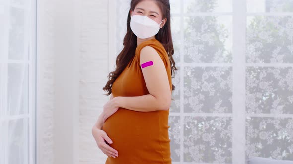 Pregnant Asian Woman wear face mask received anti virus vaccine cheerful with bandage