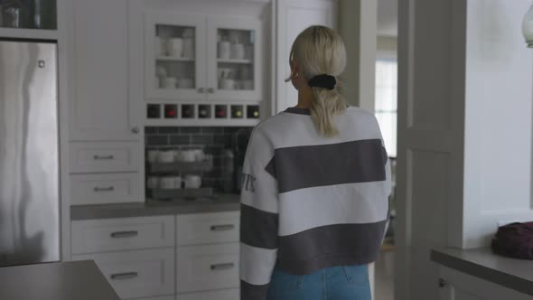 Woman walking to the cabinet to grab a mug to make a cup of coffee.