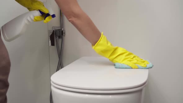 Women's Hands in Yellow Gloves Wipe the Toilet Bowl in the Bathroom with a Rag