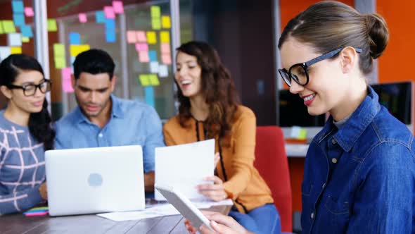 Smiling female executive using digital tablet while colleagues discussing over laptop