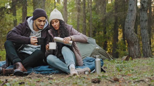 Young Couple in Love Travelers Sits in Nature Resting Drinking Tea From Thermos Enjoy Hot Drink