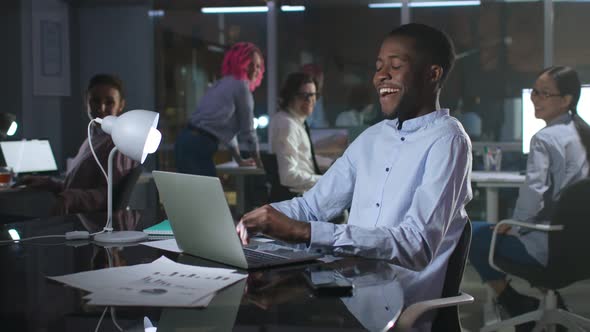 Happy AfricanAmerican Businessman Work on Laptop and Laugh Late in Office