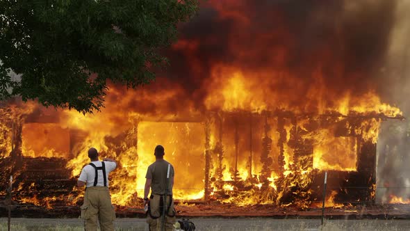 Firemen watching house on fire as it burns in slow motion