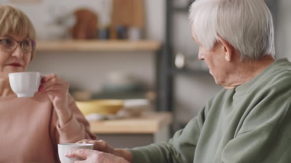 Senior Woman Reading News Online and Talking with Husband over Tea