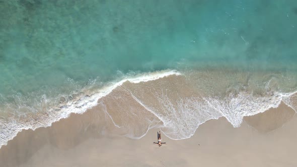 Aerial top down of relaxing woman at seashore and crystal clear water of Gili meno Island during sun
