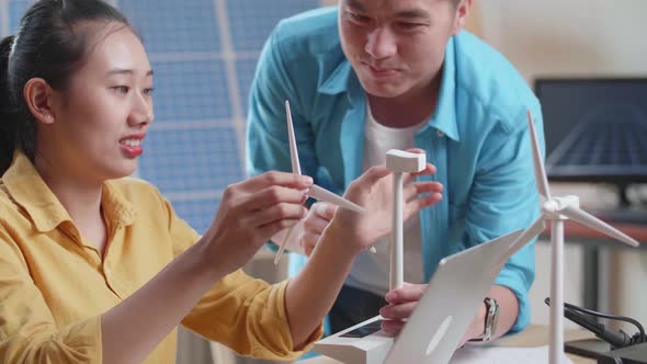 Man And Woman Assemble The Wind Turbine While Working With Laptop Next To The Solar Cell