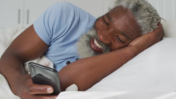 Senior man having a video chat on his smartphone in bed at home