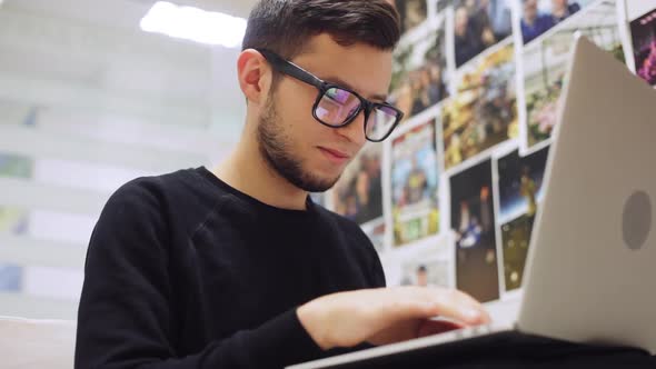 Close-up Shot of Young Stylish Businessman in Glasses, Typing on His Smartphone and Laptop, Against