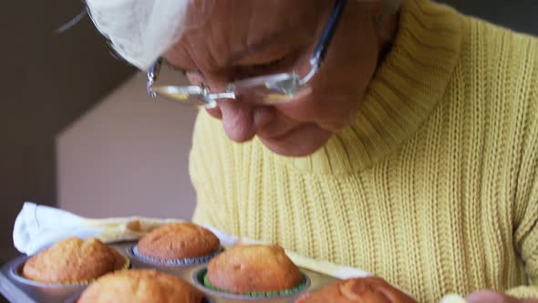 Senior woman smelling freshly baked muffins in the tray 4K 4k