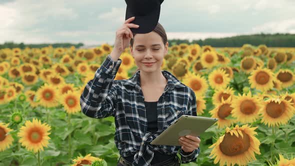 An Female Farmer Stands in Field of Sunflowers and Puts on a Cap Investigating Plants Ecologist