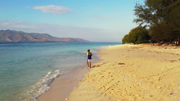 Fishing for cool teenager on a trip hanging out on beach on clean white sand and blue 4K background