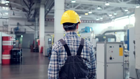 Shot of Professional Factory Worker Wearing Hard Hat Holds Tablet Computer Walking Through Modern