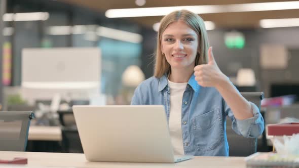 Thumbs Up By Young Woman with Laptop at Work