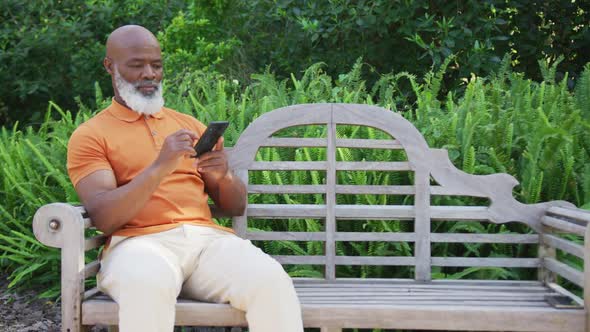 African american senior man using smartphone while sitting on a bench in the garden