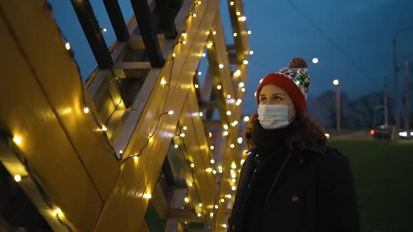 Sad Young Woman in Medical Mask and Xmas Hat Checks Decorations