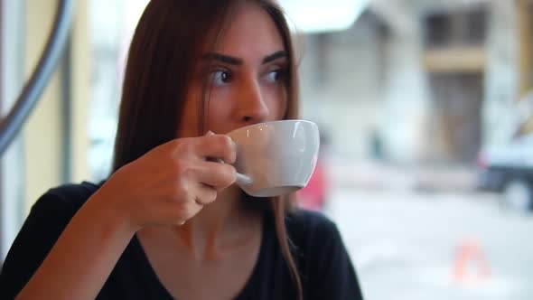 Closeup View of Attractive Young Woman Dreaming with Cup of Hot Coffee Sitting By the Window in the