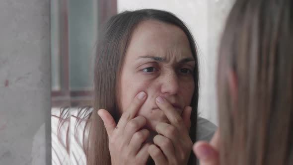 Young Woman is Looking on Her Pimples in Face Skin in Mirror