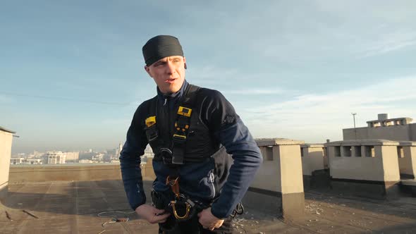 Sporting European Male Industrial Climber in Uniform Attaches Various Hooks and Cable Ties To His