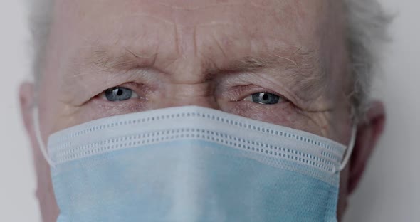 Macro Portrait of Serious Senior Man in Mask Looking Into Camera on Background