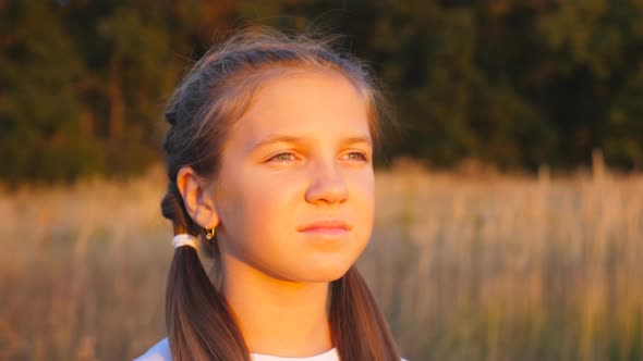 Portrait of Happy Smiling Girl Stands at Grass Meadow Looking at Beautiful Evening Sunset