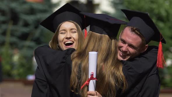 Friends Graduates in Academic Dresses Congratulating and Hugging Each Other