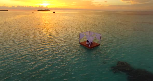 Aerial drone view of a man and woman having dinner on a floating raft boat at sunset.