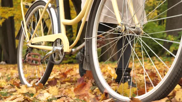 Young Woman in Boots Rolls a Bicycle Through Fallen Autumn Leaves Closeup