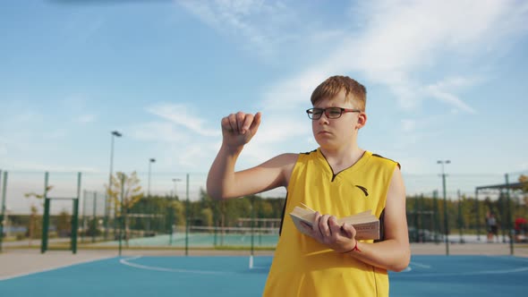 Serious boy with book calculating on the basketball court
