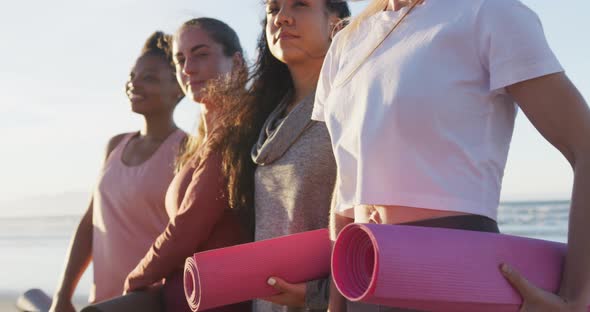 Group of diverse female friends holding yoga mats at the beach