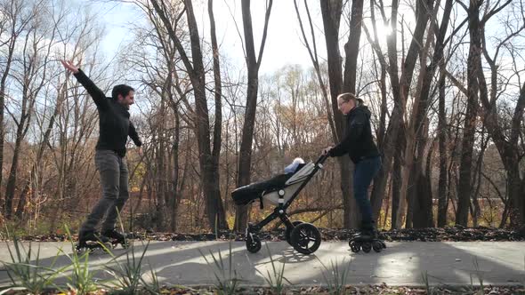 Happy Family. Young Parents Roller Skating with a Child in a Stroller in a City Park. Autumn Sunny