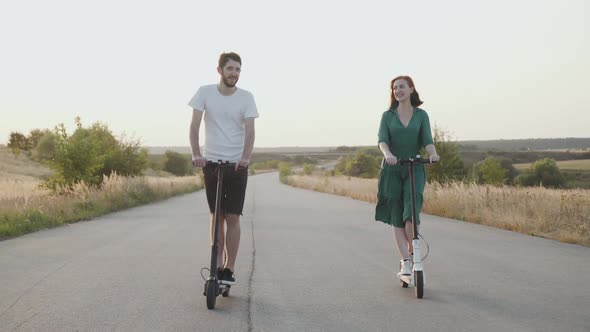 Couple in Love Riding on Electric Scooters to the Camera on the Way Out of Town