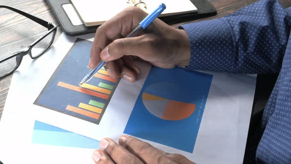 Man Hand with Pen Analyzing Bar Chart on Paper 