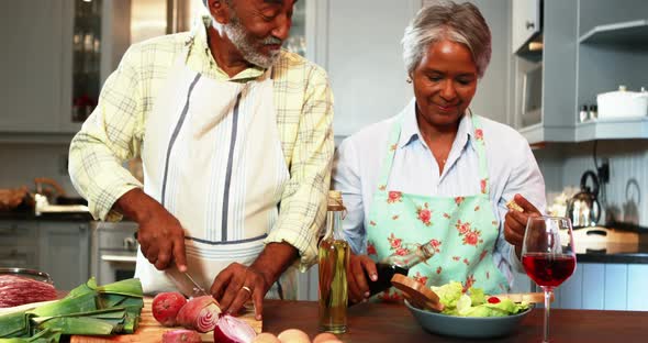 Senior man chopping vegetables while woman preparing salad in kitchen