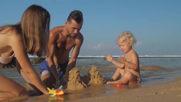 Family Plays on Beach Enjoying Holiday Against Oceanscape