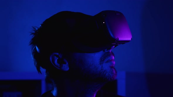 Close-up of a bearded man's head in a VR helmet in a dark room with blue light