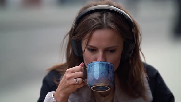 Woman Is Sipping Hot Coffee From Cup in Street Cafe, Closeup Portrait in Slow Motion, Using