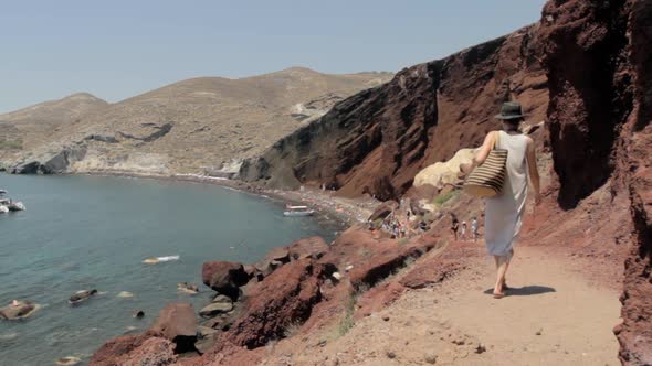 A woman follows the path that leads to the red beach that is visible in the background.
