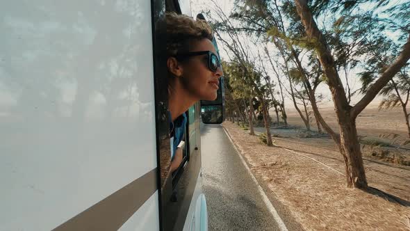 beautiful caucasian young woman travel outside the camper van with wind in the curly hair travel