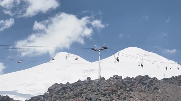 Tourists Slowly Climb the Old Chairlifts Uphill Against the Background of Elbrus