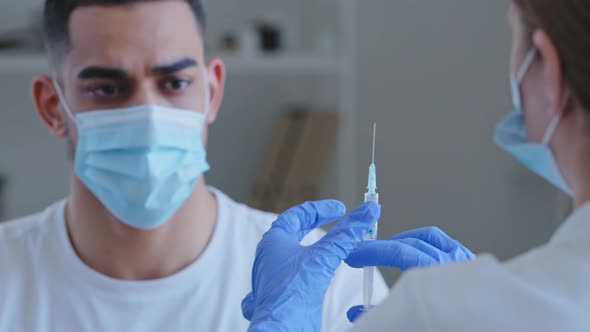 View From Behind Woman Doctor Nurse Holding Syringe with Drug Vaccine for Covid Male Patient