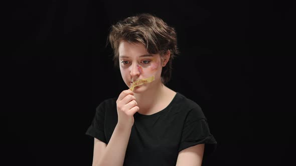 Brunette Young Woman with Brown Eyes and Beaten Face in Bruises Taking Off Stop Violence Sign From