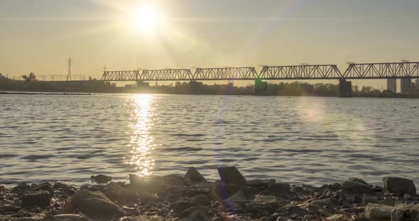 Timelapse of City River Bank. Sun Rays, Blue Sky and Railway Bridge Over Horizont. Summer Sunset