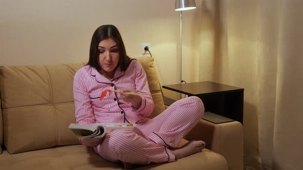 Woman Brunette Reads a Book and Eats Rolls in the Evening